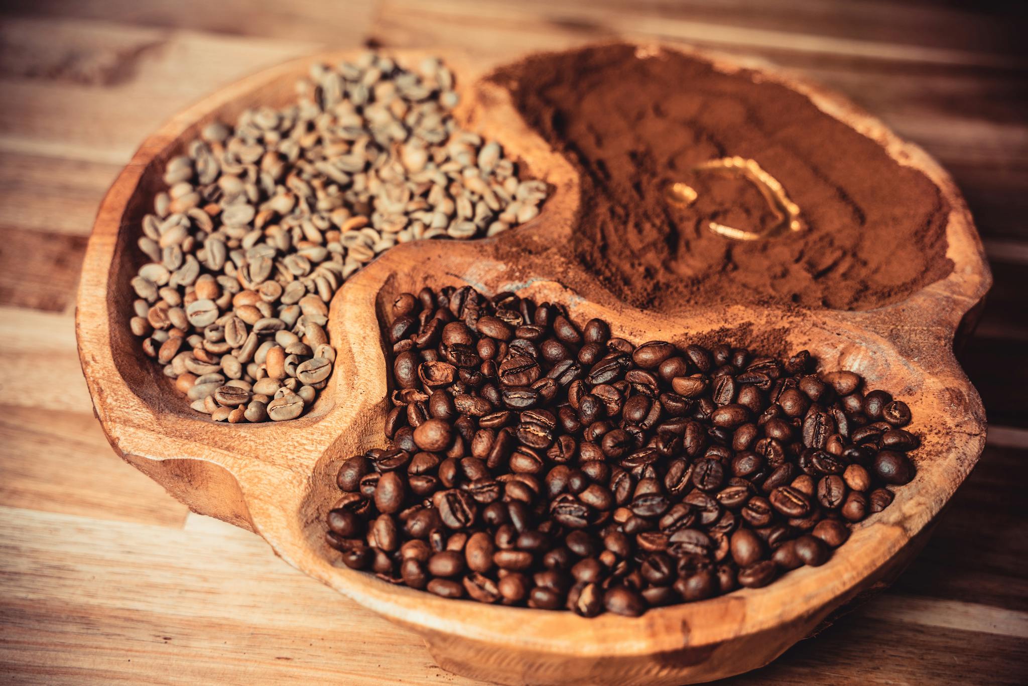 Artistic close-up of raw, roasted, and ground coffee on a uniquely carved wooden tray.