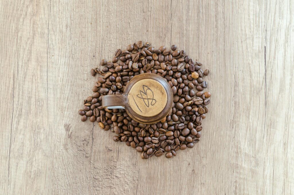 Overhead view of a wooden mug surrounded by coffee beans on a rustic wooden table.